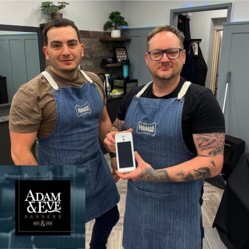 Two men in barber aprons holding a card machine.